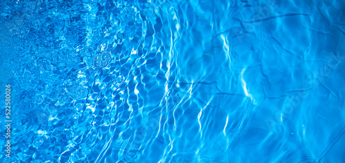 Photo of water in a blue pool. Background of clear blue water. Refreshing freshness of water.A rectangular banner with a splash of water in the pool.