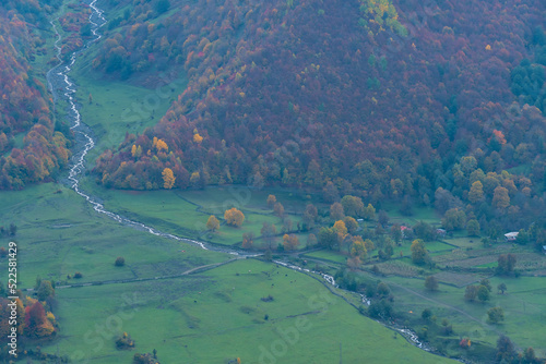 River flowing down from the mountain along the village at the foot of the greatest Caucasus mountains on an autumn day. Beautiful landscape of autumn mountains