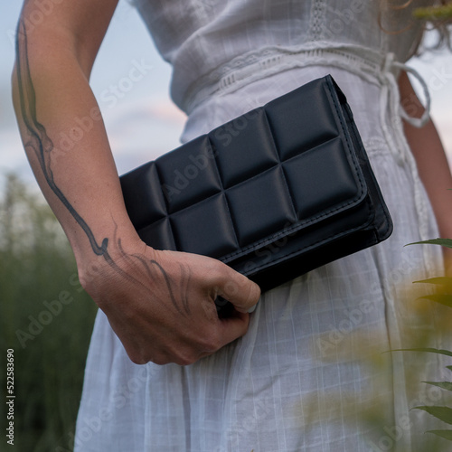 Woman holding qulted black clutch at natural green background.