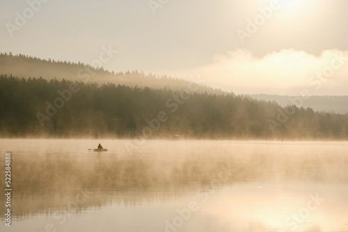 a fisherman in a boat catches fish in the early foggy morning
