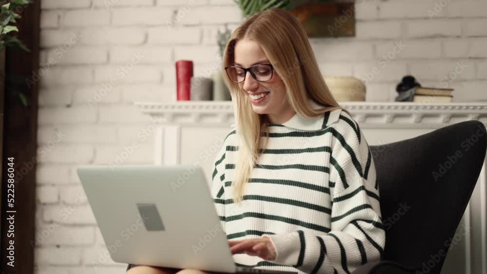 Attractive blonde woman using laptop while sitting on the chair in the living room and show thumbs up. Girl recommend it. Attractive blonde woman using laptop while sitting on the chair in the living room and show thumbs up. Girl recommend it.