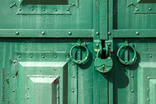 The metal gate is padlocked. Rusty padlock on the gate, close-up. Rough iron doors painted green. © Vladimir
