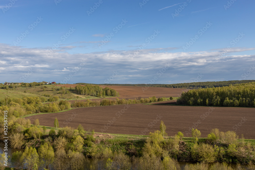 View of the countryside. bright greenery in the ravine. Saturated green grass against the blue sky. Plowed field on the horizon.