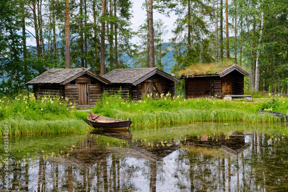 Old houses and boat on the lake in the open-air museum in Norway, wooden walls and grass roof Old houses and boat on the lake in the open-air museum in Norway, wooden walls and grass roof