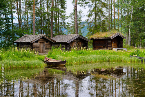 Old houses and boat on the lake in the open-air museum in Norway, wooden walls and grass roof