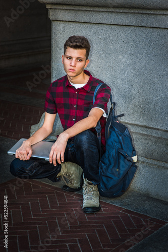 Obraz na płótnie Young man wearing short sleeve, black, red patterned shirt, jeans, boot shoes, carrying shoulder bag, holding laptop computer, squatting on corner of street in New York City, sad, relaxing, thinking. w salonie
