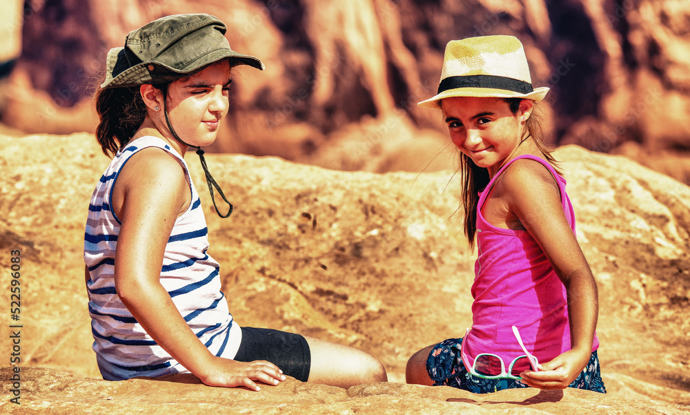 Two young girl wearing straw hats seated on a national park rock under the sun.