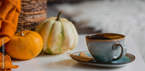 Cozy autumn concept. Home warmth in cold weather. Still-life. A blanket, pumpkins, flowers and a cup of tea on the coffee table in the living room home interior.