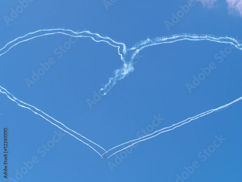 Gliders flying across the clear blue sky left heart shaped trails. Hearts in the sky