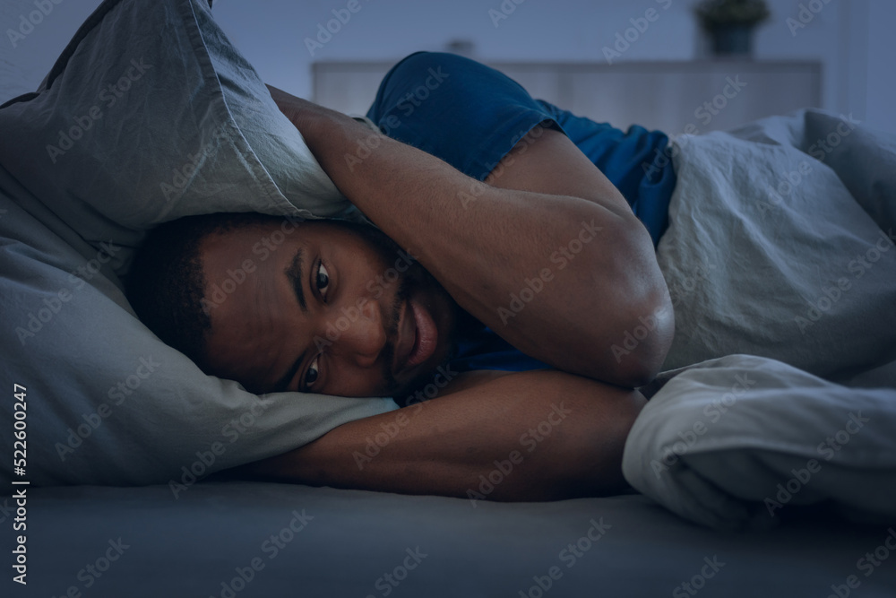 © Prostock-studio - Black Man Having Insomnia Covering Ears With Pillow In Bedroom © Prostock-studio - Black Man Having Insomnia Covering Ears With Pillow In Bedroom