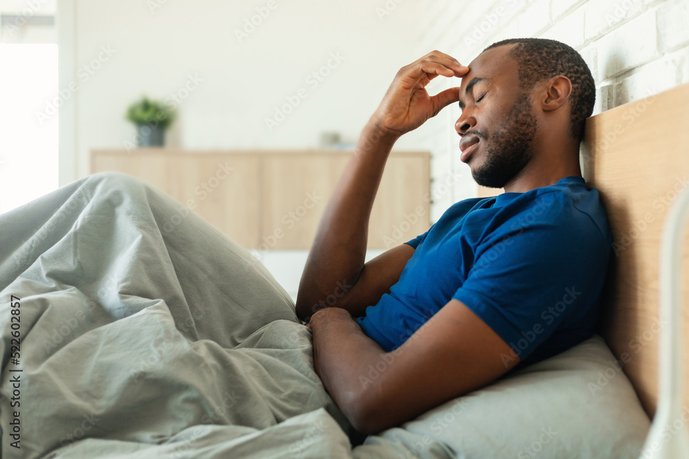 African American Man Having Headache Sitting In Bed In Bedroom African American Man Having Headache Sitting In Bed In Bedroom