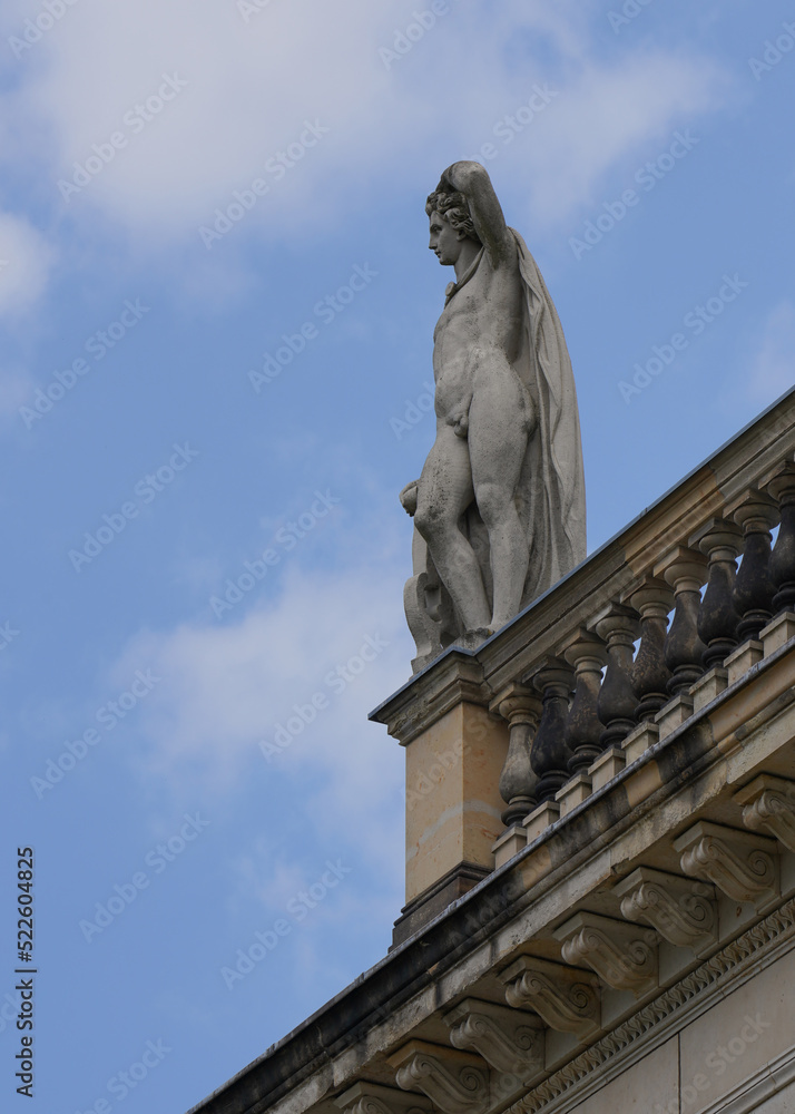 Stone, light statue on the roof of the building. Naked, young man.Art against the blue sky and clouds.Pensive image.Look into the distance.Architecture in the city .History