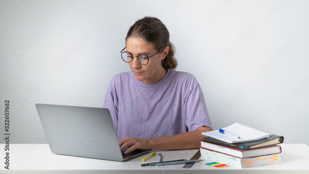 A woman prints on a laptop at a table with books and notebooks A woman prints on a laptop at a table with books and notebooks