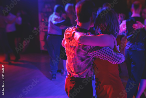 Couples dancing traditional latin argentinian dance milonga in the ballroom, tango salsa bachata kizomba lesson in the red and purple lights, dance festival