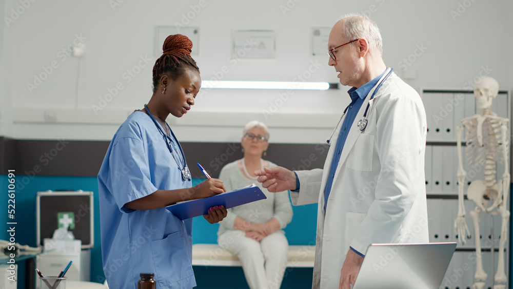 Obraz premium Multiethnic team of doctor and nurse looking at diagnosis results to give treatment and medicine to senior woman in medical cabinet. Health care expertise to cure sickness at checkup.