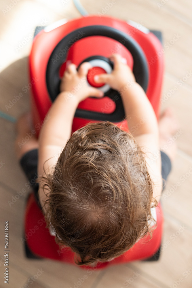 Naklejka premium Baby boy, caucasian, one year old, riding a push car. Top view, indoor. Vertical, selective focus.