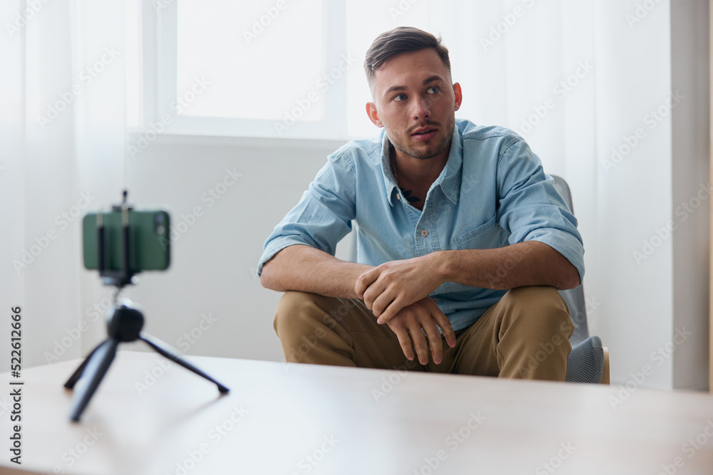 Serious self-confident cheerful attractive influencer blogger reclines on knee looks aside using phone for recording video lesson at home. Copy space. Gadget addiction Online education concept Serious self-confident cheerful attractive influencer blogger reclines on knee looks aside using phone for recording video lesson at home. Copy space. Gadget addiction Online education concept