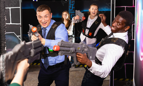 Cheerful positive smiling men and women in business suits playing laser tag emotionally in dark room