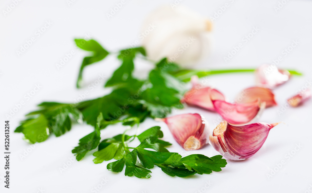Closeup of fresh green sprig of parsley and unpeeled garlic cloves on white background, selective focus