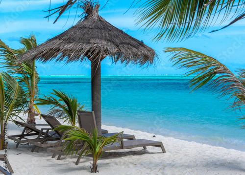 Fototapeta Naklejka Na Ścianę i Meble -  Beautiful tropical beach with white sand and two sun loungers on background of turquoise ocean and blue sky with clouds. Luxury resort in Maldives 2022