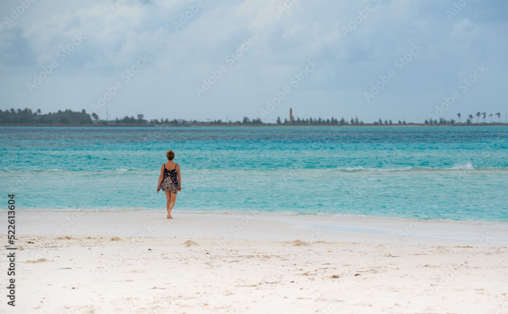 Woman walking along the beach with turquoise water, in tropical paradise, in Maldives Island 2022