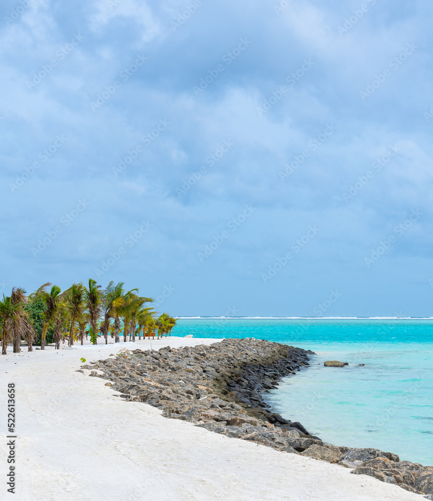 Beautiful bay breakwater, with rocks, white sand, palm trees, turquoise water and blue sky in tropical Maldives island