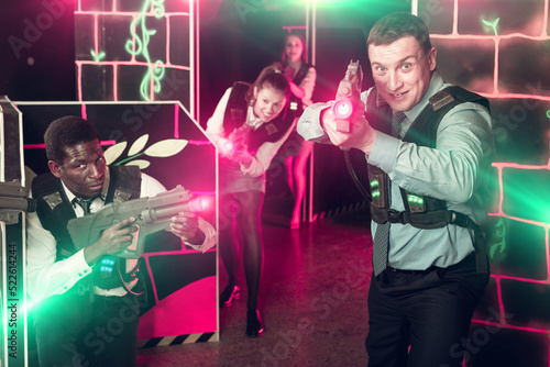 Pleasant smiling positive men and women in business suits playing laser tag emotionally in dark room
