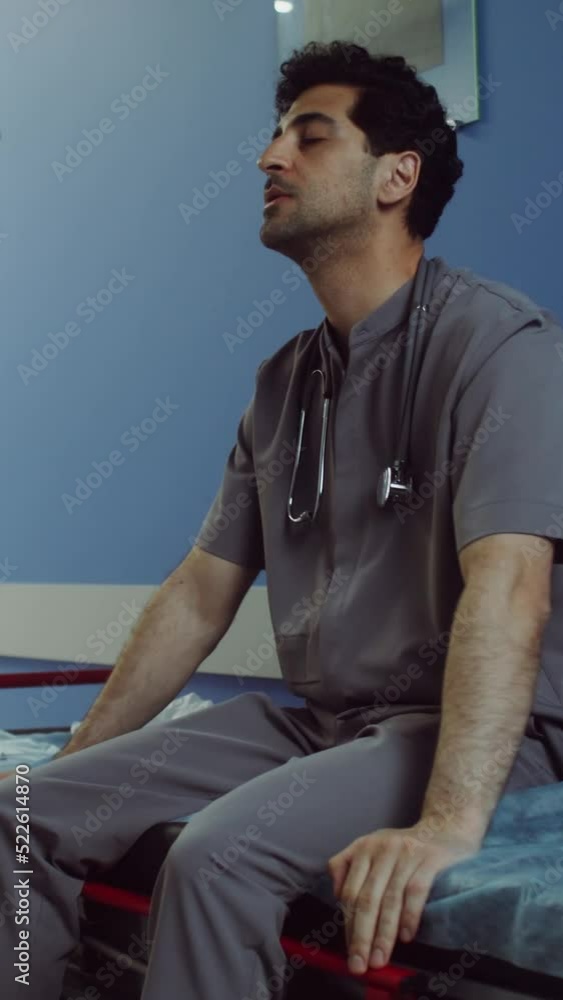 A doctor sits on a medical gurney and rubs his head in empty hospital corridor A doctor sits on a medical gurney and rubs his head in empty hospital corridor