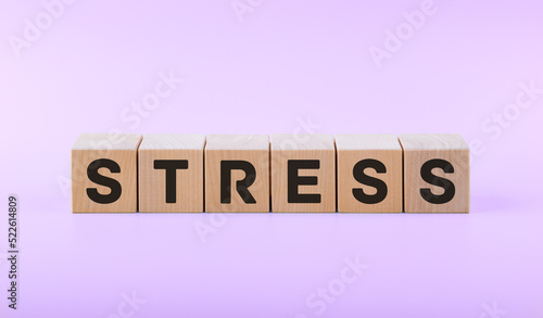 Text STRESS on wooden cubes on a pink background.