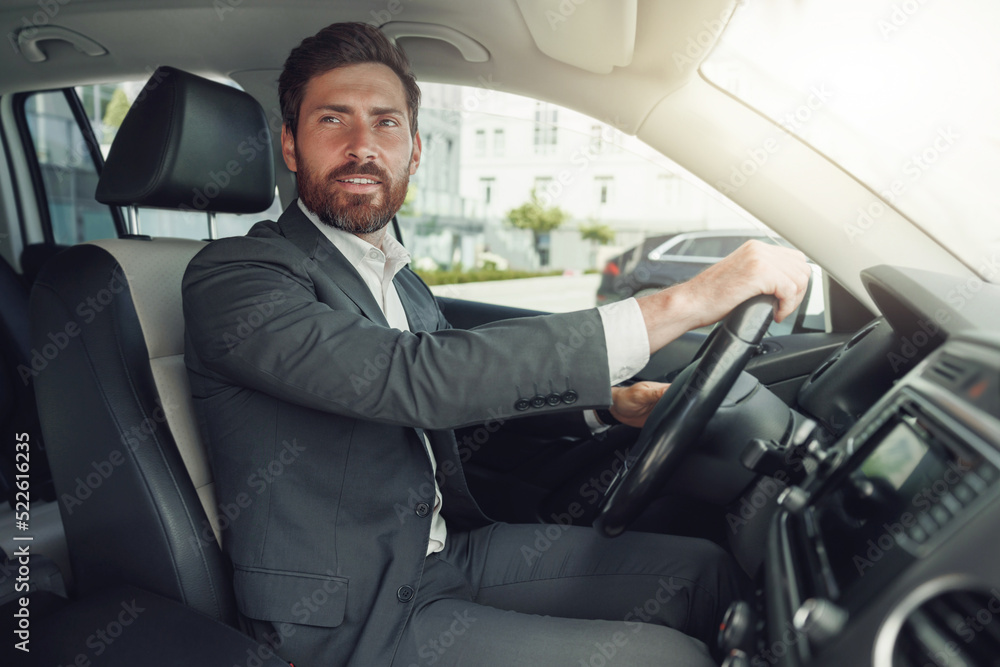Handsome businessman in grey suit is riding behind steering wheel of car Handsome businessman in grey suit is riding behind steering wheel of car