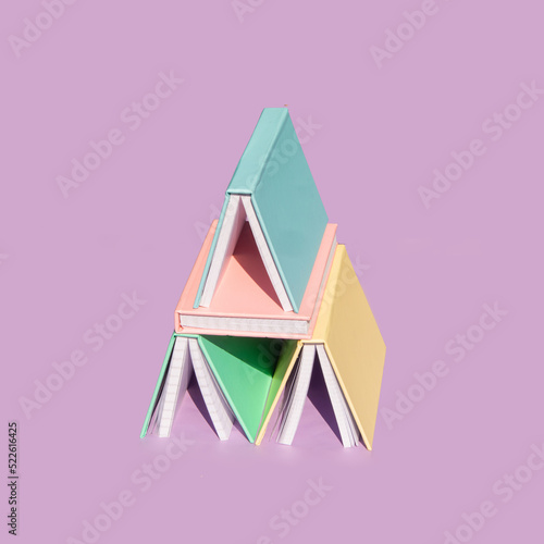 Creative back to school concept. Colorful book tower on pastel bright purple background. Minimalistic education composition.