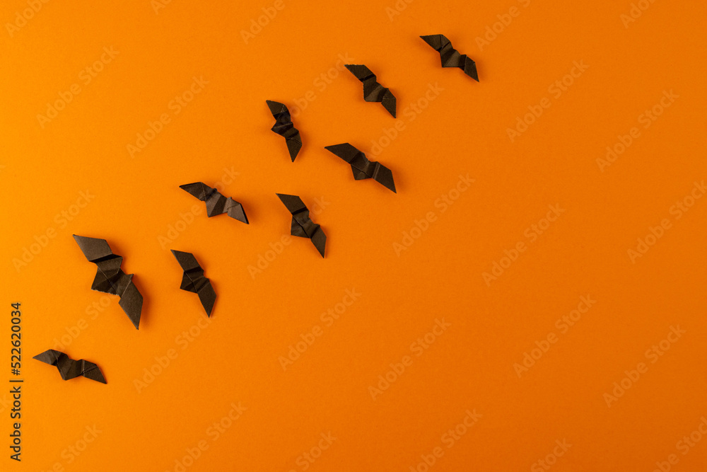 Black origami bats on orange background. Orange and black paper halloween background Black origami bats on orange background. Orange and black paper halloween background