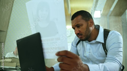 Detective processing case documents in laptop at police department. Serious cop comparing photo with information in computer sitting at the table.High quality 4k footage