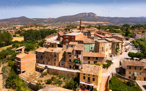 Scenic aerial view of ancient Spanish town of Figuerola dOrcau with tile-roofed houses nestled together on top of hill against mountain range on horizon on sunny summer day, Catalonia photo