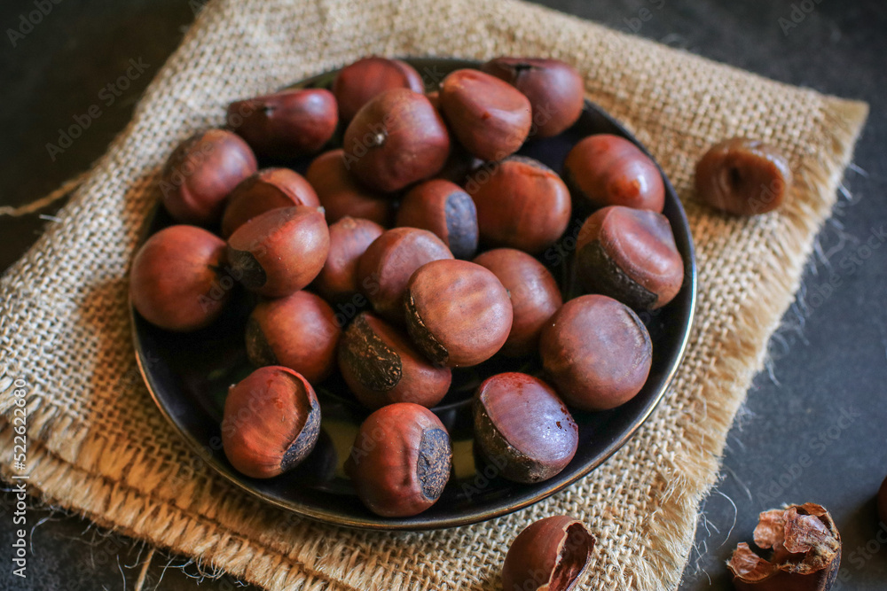 Chestnuts in black bowl over grey background. Pile of fresh chestnuts ready to roast. Top view, copy space. Chestnuts in black bowl over grey background. Pile of fresh chestnuts ready to roast. Top view, copy space.