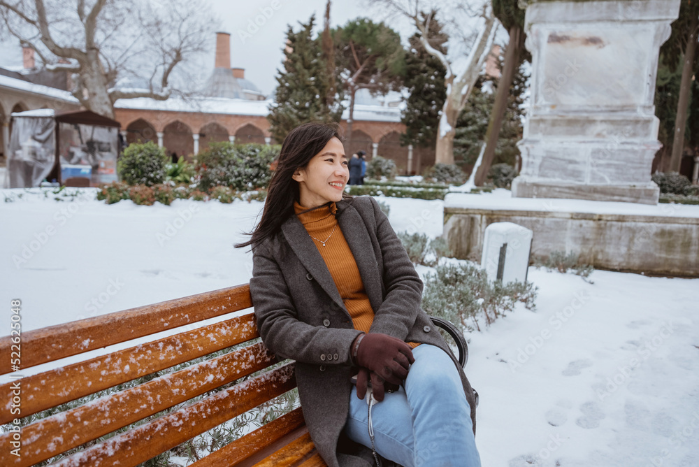 beautiful young woman sitting on bench in the park during snowy day