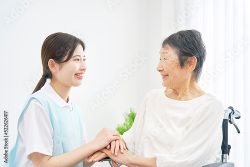 介護施設で車椅子に乗るシニア女性と会話する介護士 photo