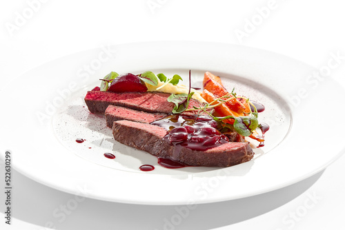 Venison steak with baked vegetables isolated on white plate. Meat steak medium rare roasted with carrot, beetroot and mashed potatoes with cherry sauce. Wild meat in restaurant menu.