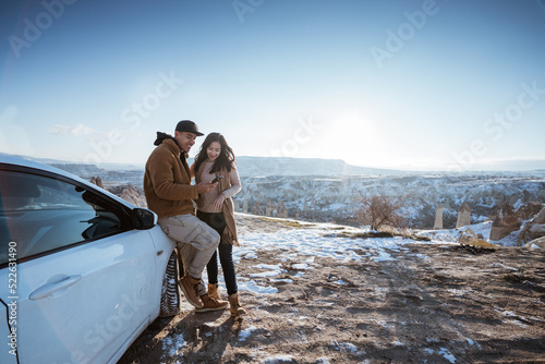 asian couple doing adventure by car looking at mobile phone with beautiful cappadocia cover with snow in the background © Odua Images