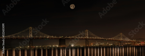 Photography San Francisco Bay Bridge with moon above and lights on at night with reflection