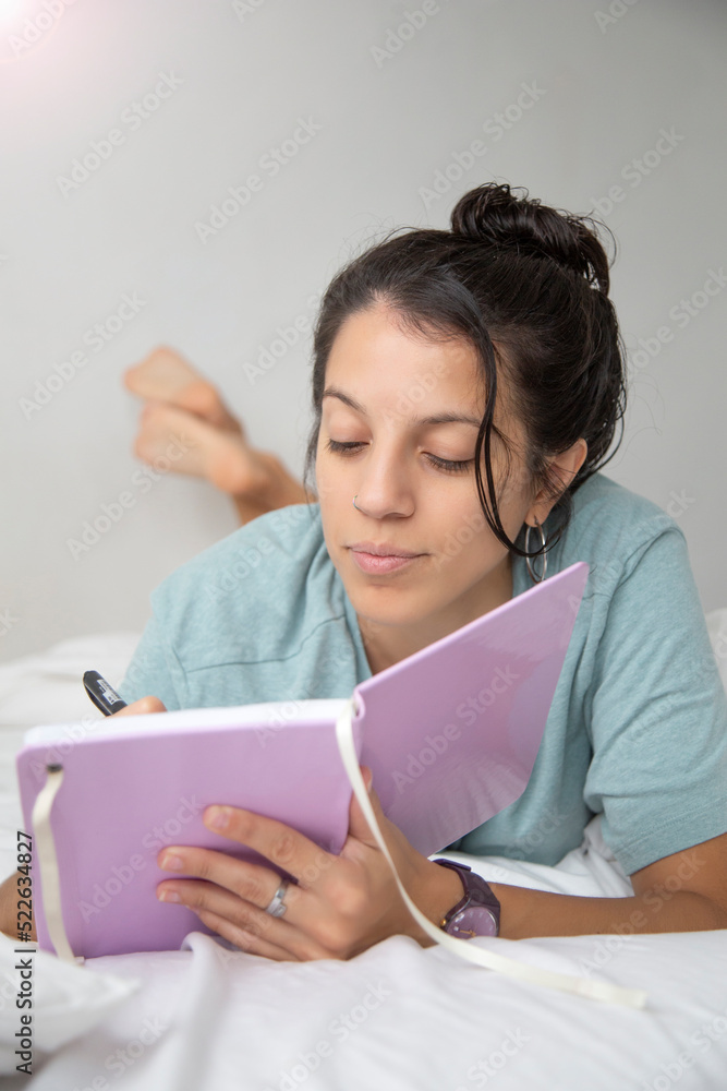 Caucasian woman wearing only a t-shirt writing in her notebook on the bed Caucasian woman wearing only a t-shirt writing in her notebook on the bed