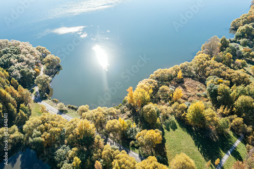 colorful trees around the lake in autumn. sunlight reflecting in tranquil water. aerial overhead view.