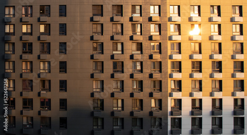 Facade of multi-storey residential building at sunset. Structure with windows reflecting the setting sun. Aerial view.
