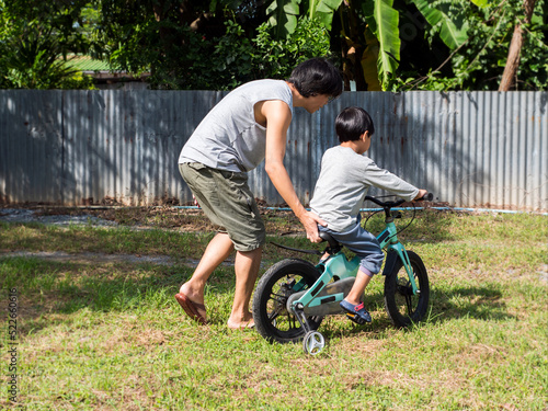 Father teach asian child boy son to ride bicycle in countryside background. Dad and young kid having sport activity and exercise together in summer, happy freedom family time. Father's day concept.
