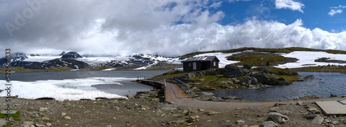 Norway mountain road with black hut and glacial lake extra wide panorama
