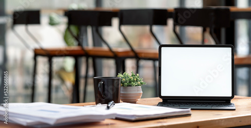 Blank white screen digital tablet with magic keyboard on wooden table in modern office room.