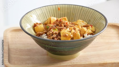 Pouring stir-fried mapo tofu with hot spicy sauce over white rice in a bowl at home photo