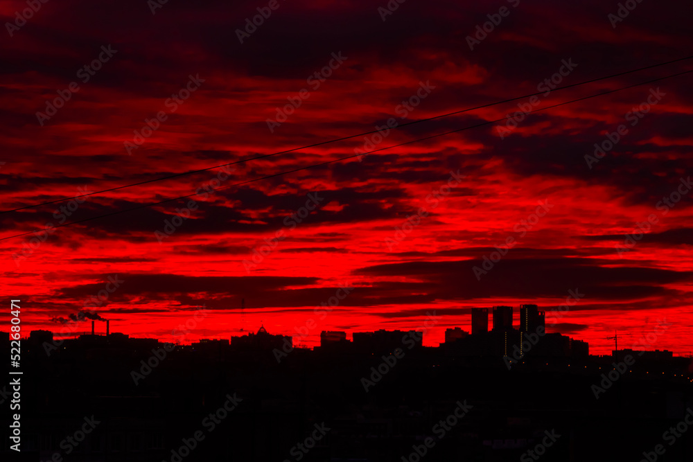 Colorful red sunrise over silhouette of city and dramatic sky with clouds - warm illumination, sun goes up. Nature, urban, morning, peaceful, atmospheric view concept