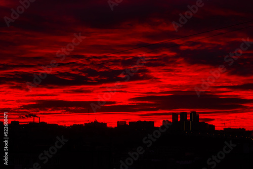 Colorful red sunrise over silhouette of city and dramatic sky with clouds - warm illumination  sun goes up. Nature  urban  morning  peaceful  atmospheric view concept