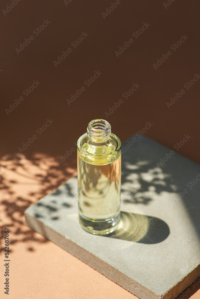 Open transparent bottle with dropper pipette with serum or essential oil and flowers shadows. Bottle on grey concrete podium for product presentation. Skincare cosmetic with wildflowers. Beauty Open transparent bottle with dropper pipette with serum or essential oil and flowers shadows. Bottle on grey concrete podium for product presentation. Skincare cosmetic with wildflowers. Beauty